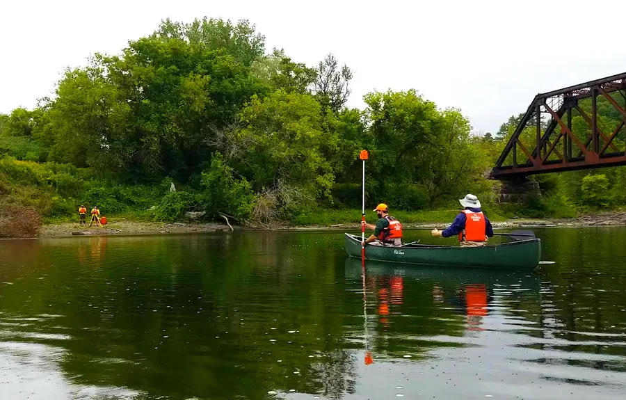 Karyawan USGS mengambil pengukuran alur sungai dari atas kano menggunakan prisma survei dan total station